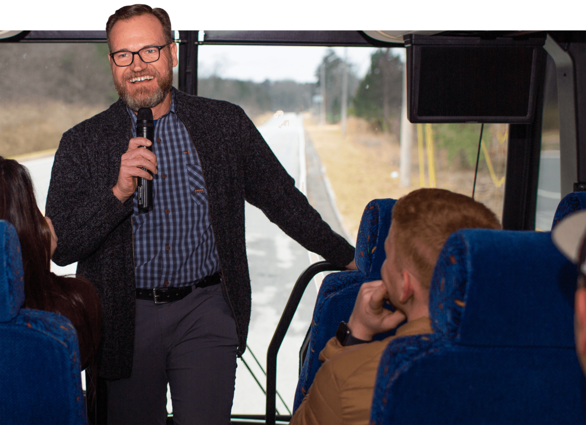A man speaks at the front of a bus