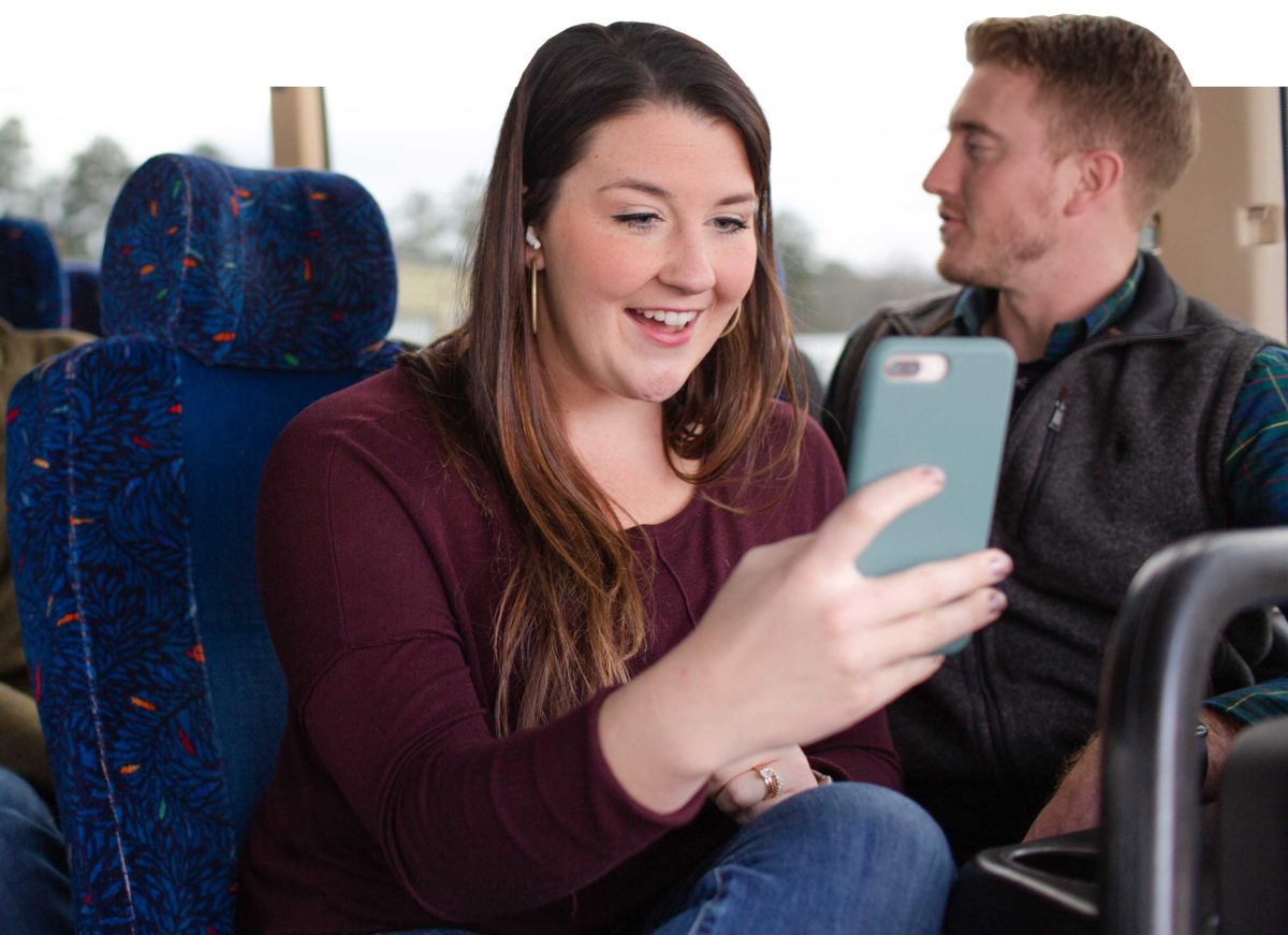 A woman looks at a phone while her seatmate talks to someone behind him