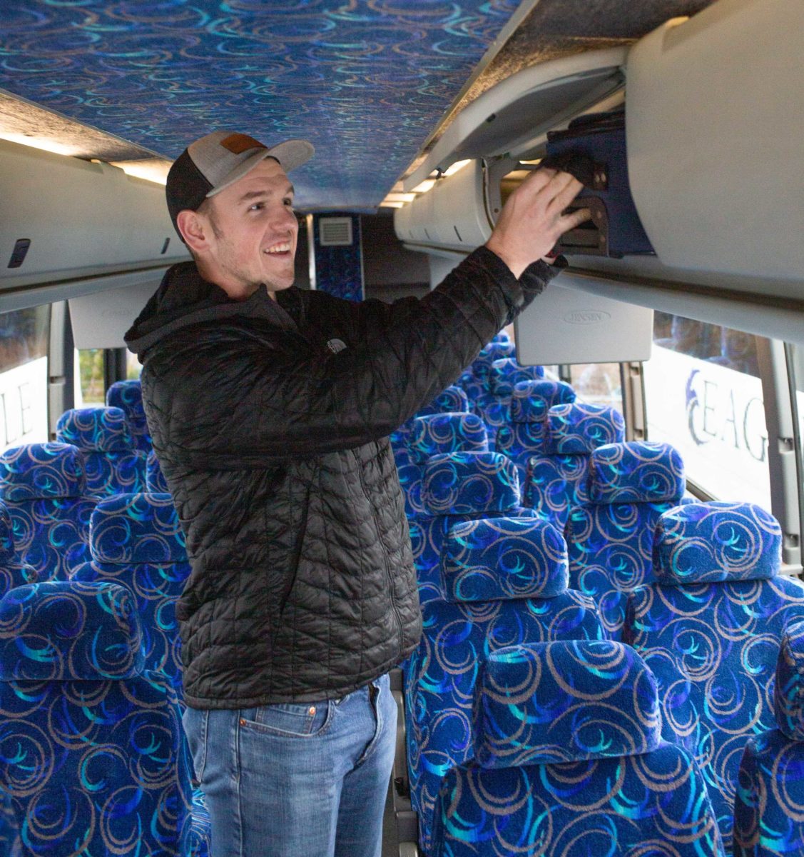 A man puts a bag in an overhead bin on a bus